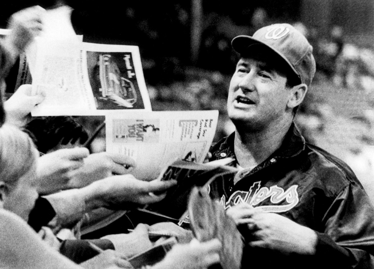 Ted Williams holds a baseball he autographed, while his son John